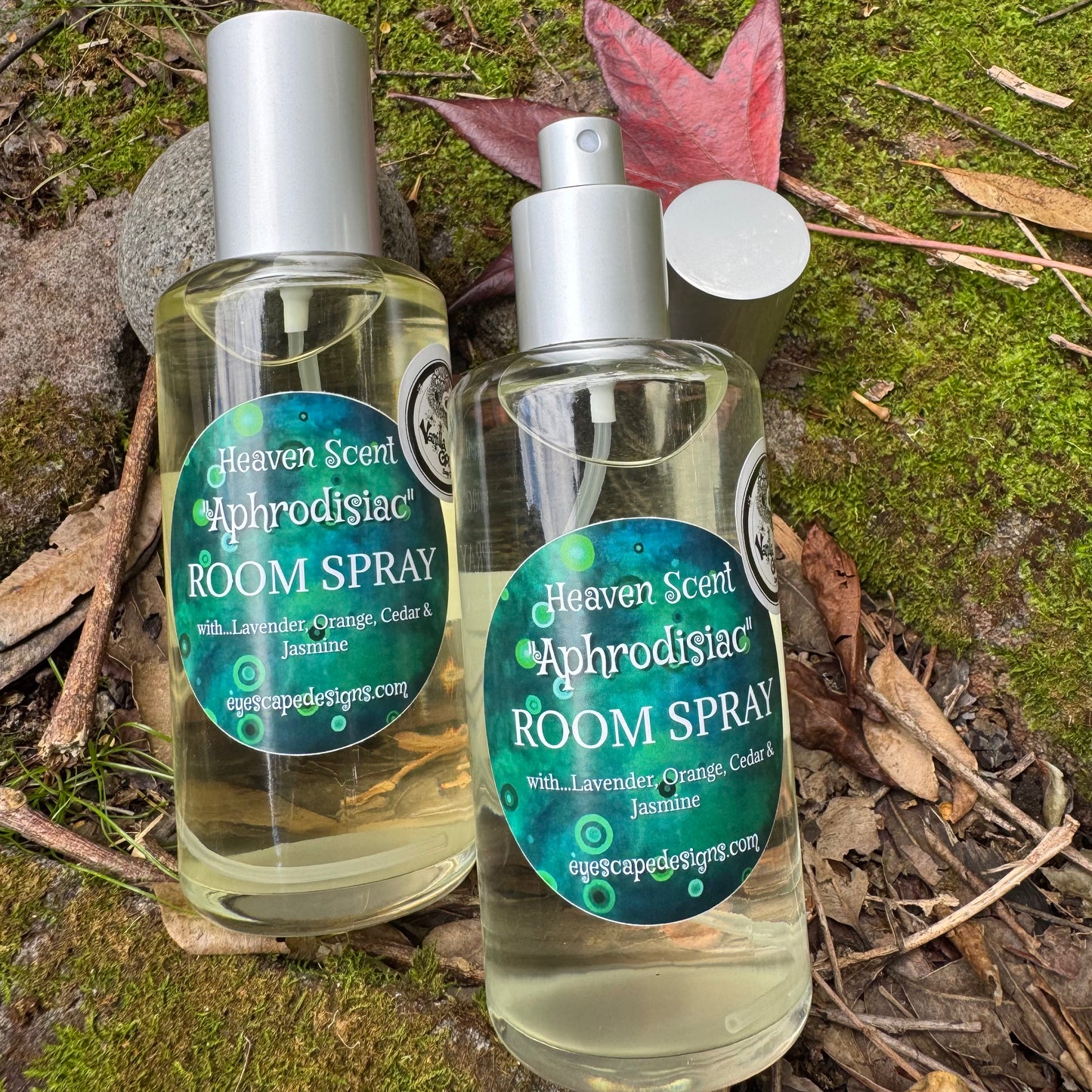 Two bottles of Heaven Scent Aphrodisiac Room Spray on a natural background with leaves and moss.