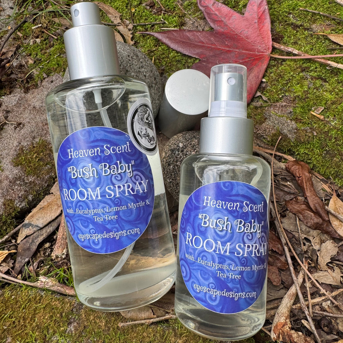 Two bottles of 'Heaven Scent Bush Baby Room Spray' on a natural background with leaves and moss.