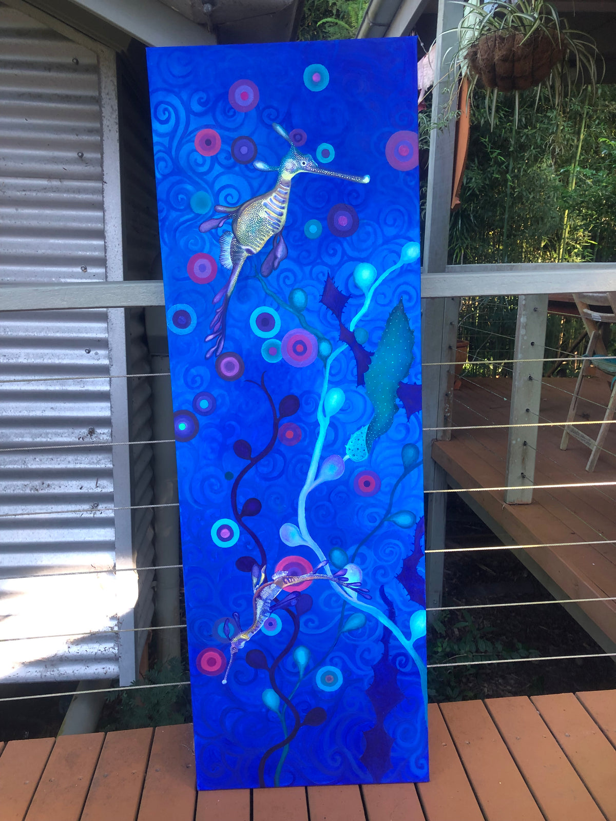 Abstract artwork of two weedy sea dragons with blue watery background and colorful patterns hanging on a wall.