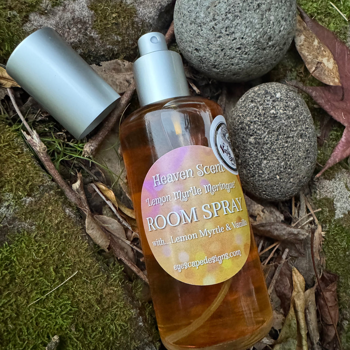 Room spray bottle labeled lemon Myrtle meringue 'Heaven Scent' on a natural background with rocks and leaves.