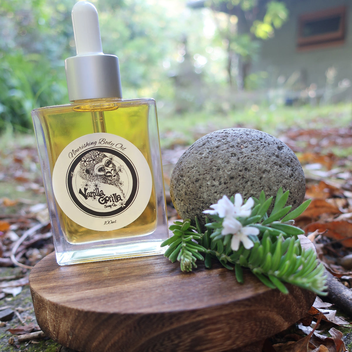 Vanilla Gorilla Nourishing Body Oil on a round wood with rock and foliage

