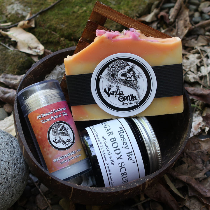 Set of body care products including a bar of soap, scrub, and deodorant in a coconut container on a natural background.