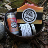 Assorted skincare products including a bar, scrub, and deodorant in a coconut on a natural background.