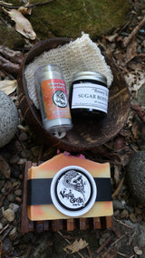 Two small bottles and a bar of soap on a natural surface with a stone and leaves.