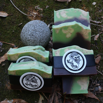 Three green camouflage-patterned soap bars with black and white circular labels on a natural background.
