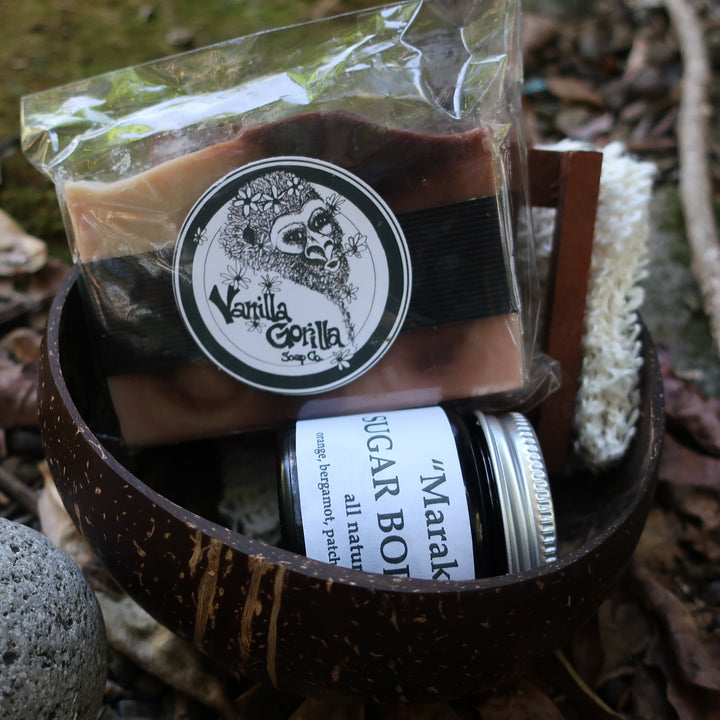 Set of natural products including a soap bar, scrubber, and jar on a stone surface with leaves.