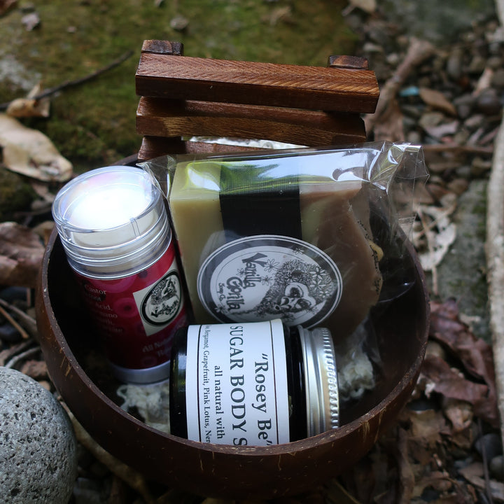 coconut bowl with soap, scrub, soap rack and deodorant with vanilla gorilla labels on a stone surface surrounded by leaves