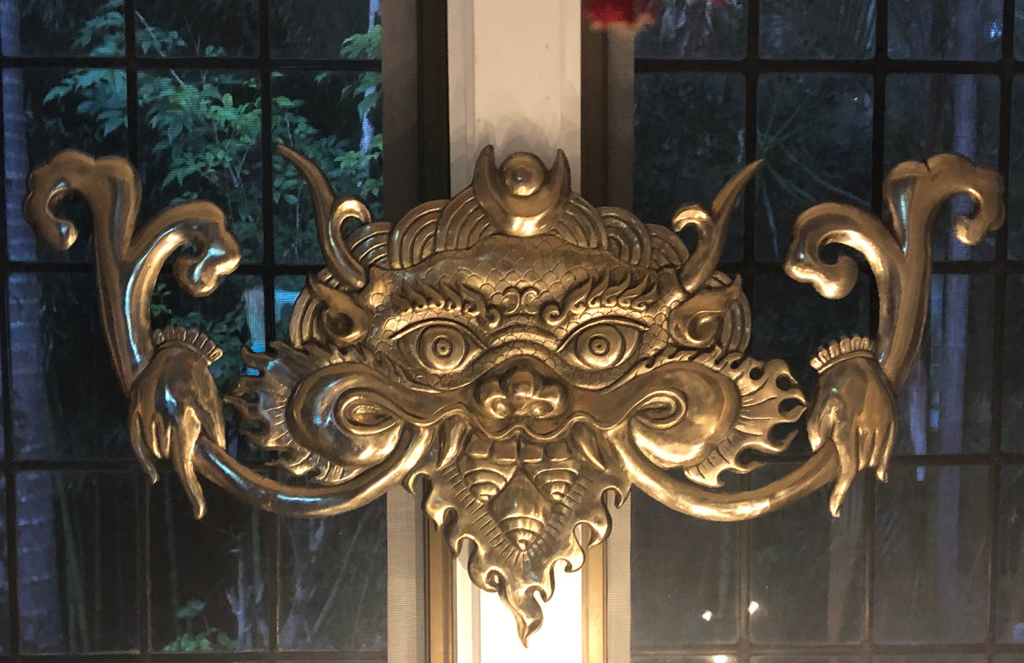 Bronze cast Kirtimukha with a shiny golden finish, displayed above a doorway.