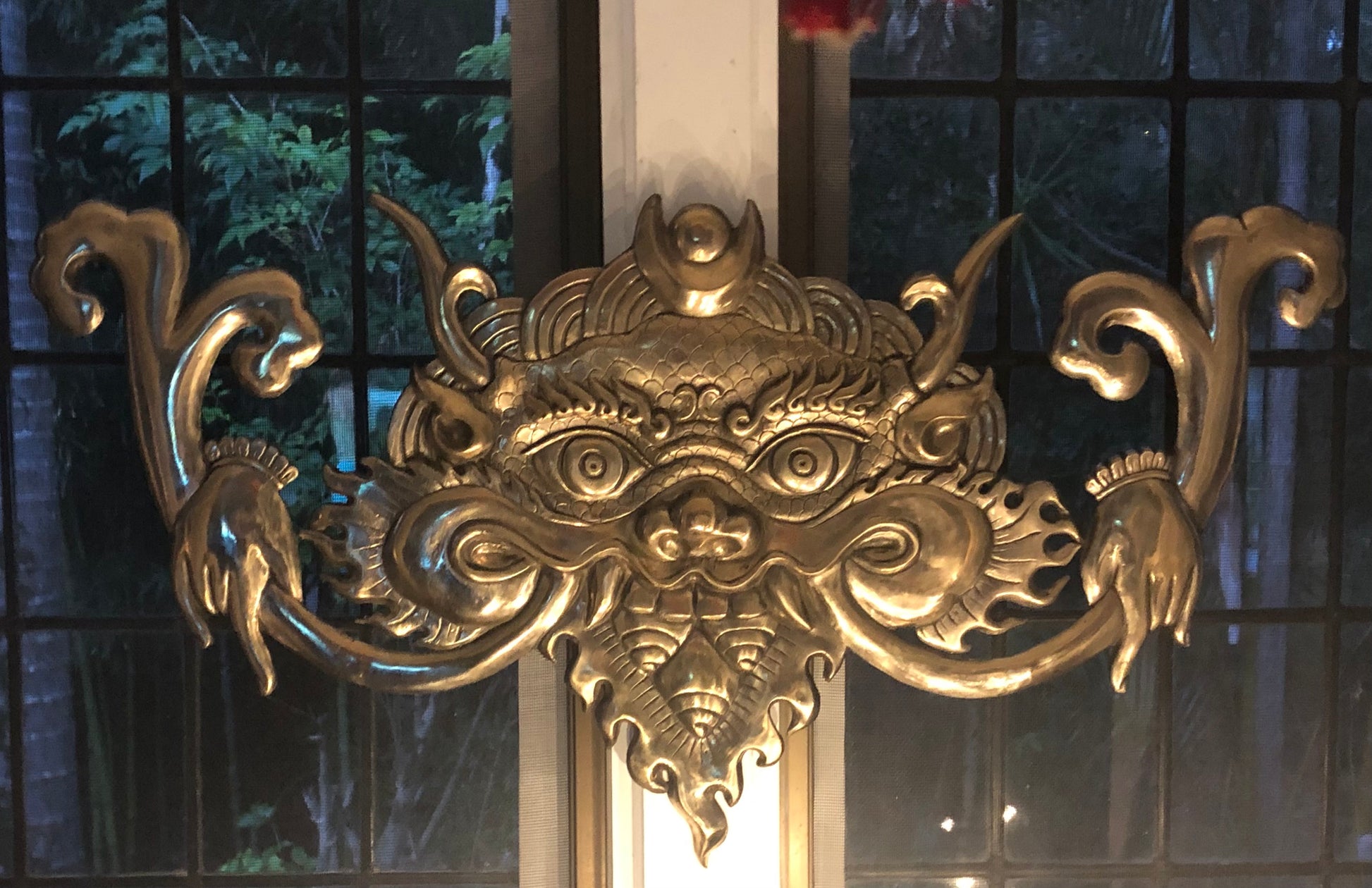 Bronze cast Kirtimukha with a shiny golden finish, displayed above a doorway.