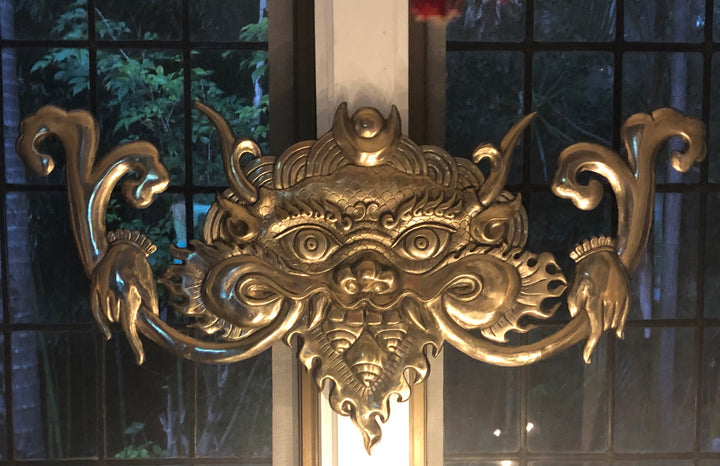 Bronze cast Kirtimukha with a shiny golden finish, displayed above a doorway.