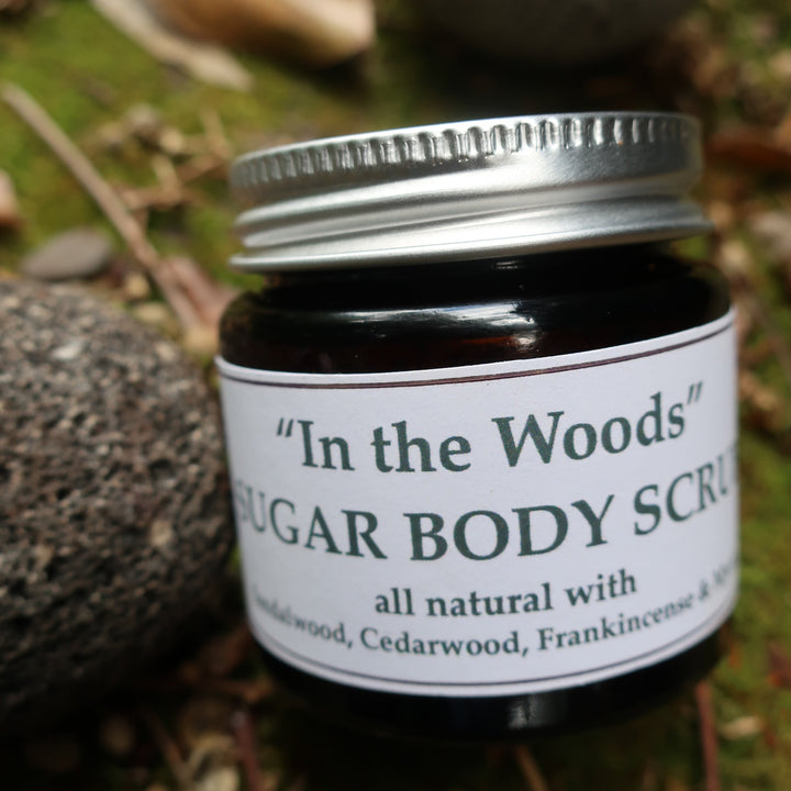 Jar of sugar body scrub labeled 'In the Woods' on a natural background