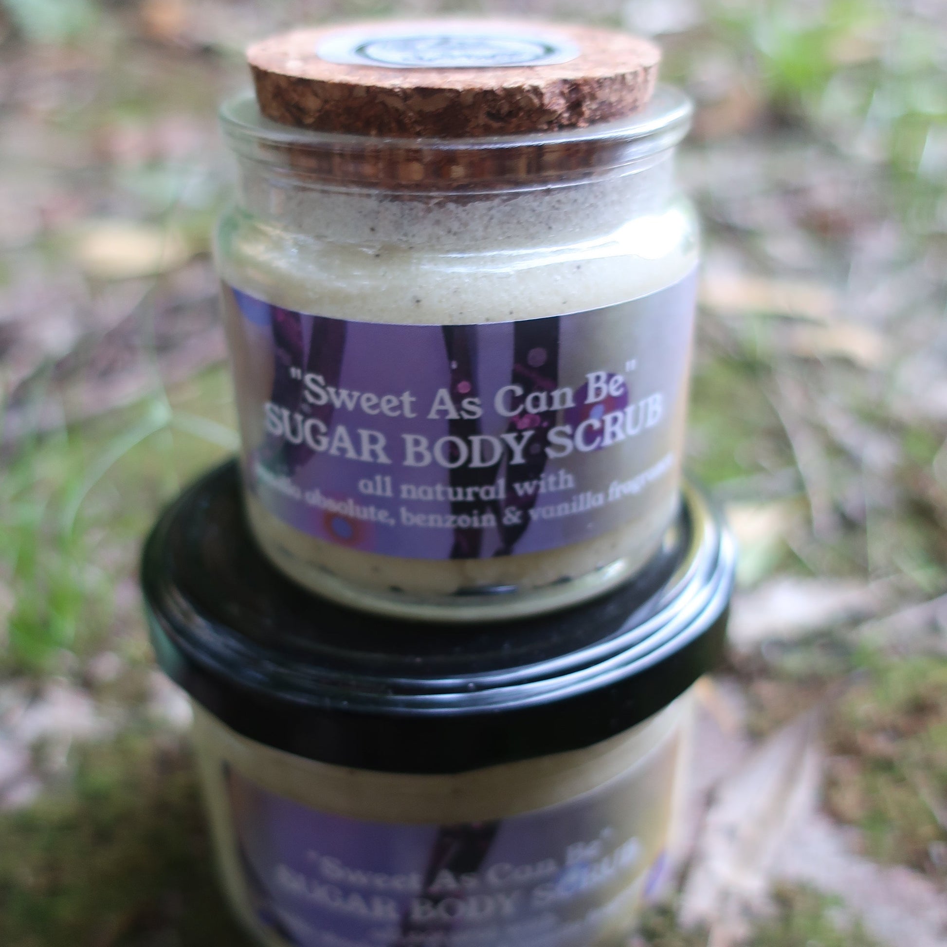 Jar of sweet as can be Vanilla body scrub with a purple label on a natural background