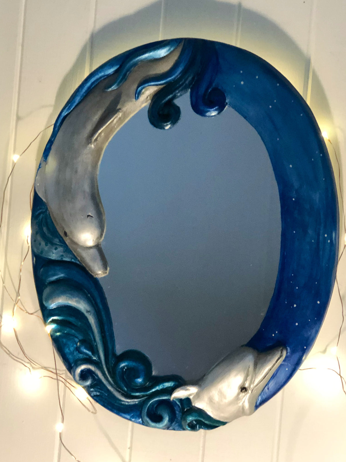 A blue decorative mirror featuring a sculpted dolphin design, with a 3D effect on the dolphins, designed to be hung on a wall.