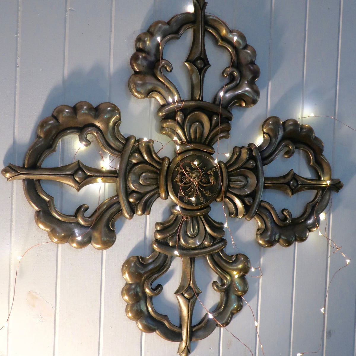 bronze double dorje vajra on a white wall with fairy lights