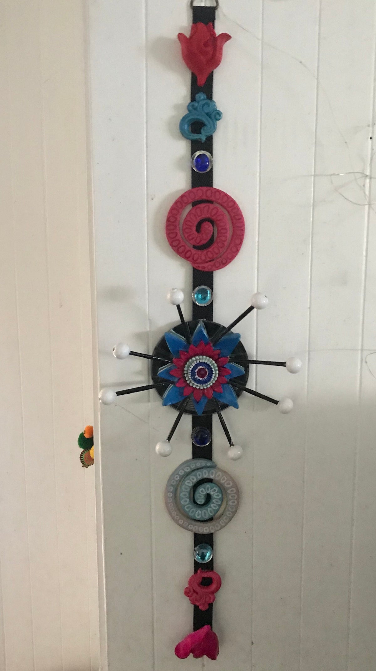 A vertical 3D wall hanging featuring a central blue flower with red and blue swirls, and round mirrors.
